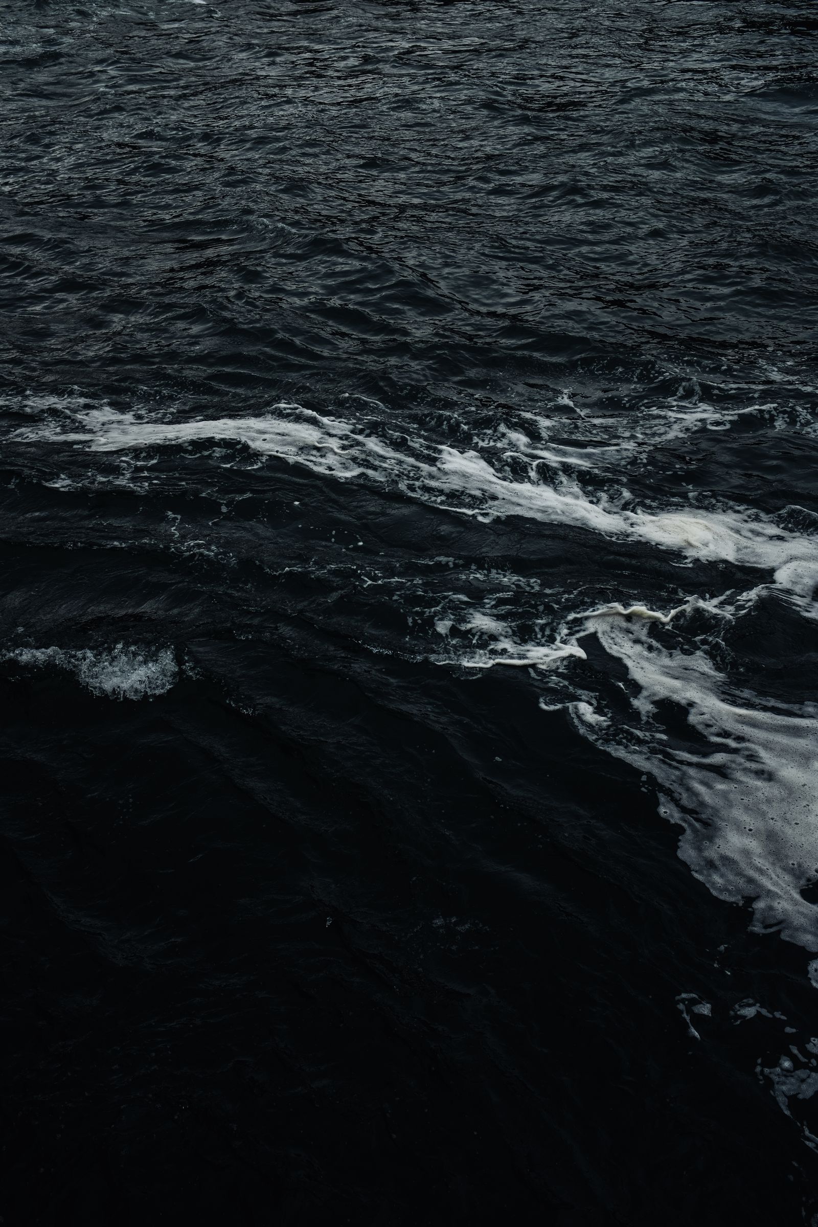 Dark liquid waves with white foam, a close abstract texture